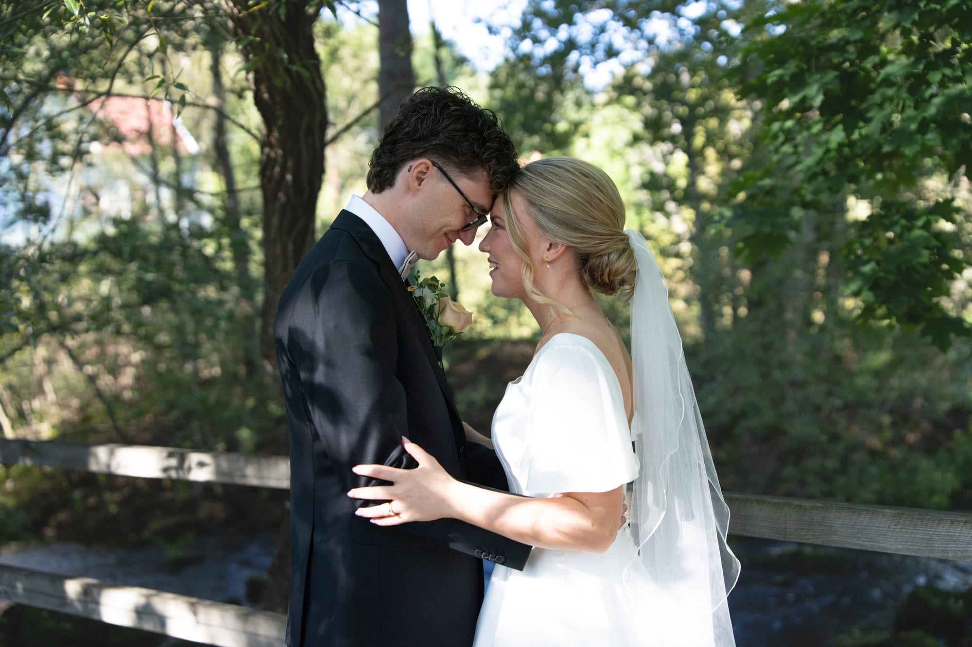 Brudparet William och Freja håller om varandra med pannorna mot varandra i varmt kvällsljus bland träd